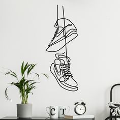 a black and white wall decal with sneakers hanging from it's side, next to a potted plant