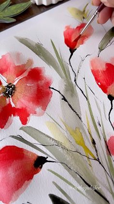 someone is painting red flowers with watercolors on white paper and using a brush