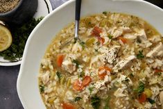 a white bowl filled with chicken and rice soup next to a plate of lemons