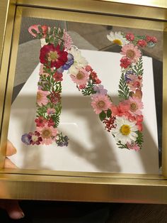 the letter h is made out of flowers in a gold frame with a person's hand holding it