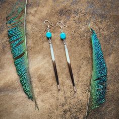 two pairs of blue and green feathers on sand