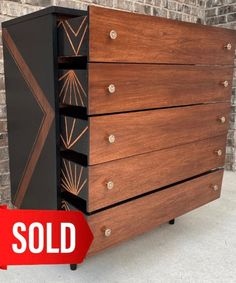 a black and brown chest of drawers sitting next to a brick wall