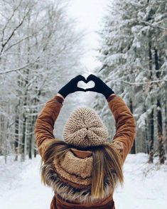 a person making a heart shape with their hands in the air while standing on snow covered ground