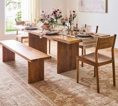 a dining room table set with place settings and flowers in vases on the table