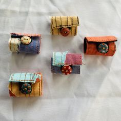 four small purses made out of fabric on a white cloth covered table with buttons