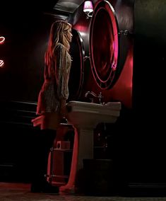 a woman standing in front of a bathroom sink with the lights on and red light behind her