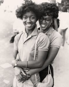 two young women are hugging each other on the street in front of some people and one is carrying a purse