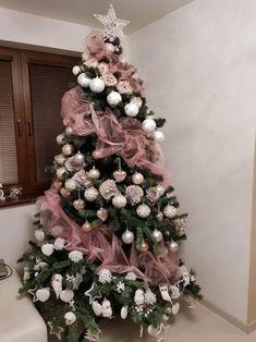 a pink christmas tree with white and silver ornaments on it's top, in the corner of a room