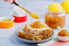 a person spooning honey from a sandwich on a plate with other food in small bowls