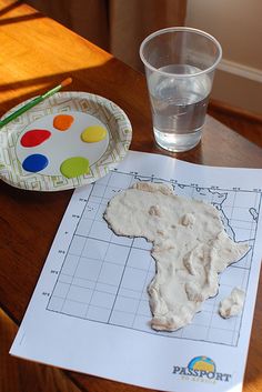 a paper plate and glass sitting on top of a wooden table next to a map