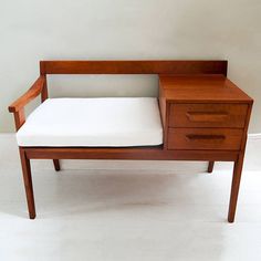 a small wooden desk with a white pillow on it's top and bottom drawer