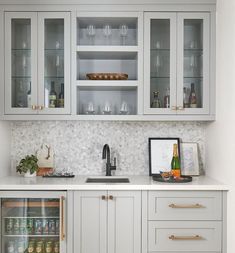 a kitchen with white cabinets and silver counter tops, wine glasses on the glass doors