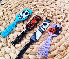 three beaded keychains are sitting on a woven basket, one has a cat and the other has a skull