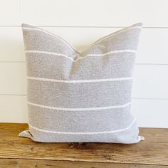 a gray and white striped pillow sitting on top of a wooden table next to a wall