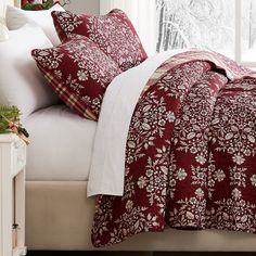 a bed with red and white comforters in front of a window covered in christmas decorations