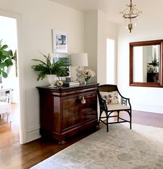 a living room with a chair, mirror and potted plant on the dresser next to it