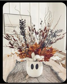 a white vase filled with lots of dried flowers and plants sitting on top of a wooden table