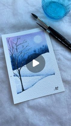 a watercolor painting of a tree in the snow next to a blue glass and pen