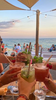 several people toasting with cocktails at an outdoor bar on the beach in front of the ocean