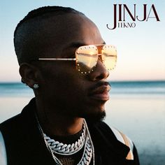 a man wearing sunglasses and chain necklaces on the beach with water in the background