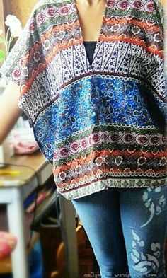 a woman standing in front of a table wearing a colorful top