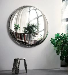 a round mirror sitting on top of a wall next to a potted green plant