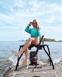 a woman sitting on top of a motor boat in the water with her legs crossed