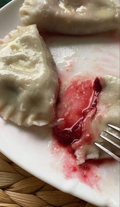 a white plate topped with dumplings covered in sauce and ketchup next to a fork