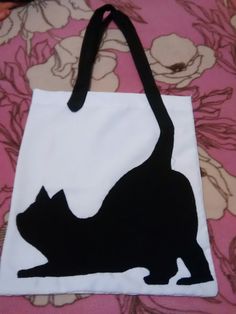 a black cat silhouetted on a white tote bag sitting on a pink flowered bed