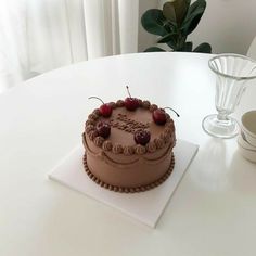 a chocolate cake sitting on top of a white table next to a glass cup and vase