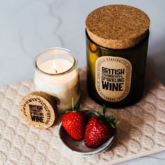 two strawberries on a plate next to a bottle of wine and a cork coaster