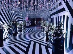 a black and white striped room with chandeliers hanging from the ceiling, flowers in vases on either side