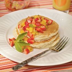 a stack of pancakes topped with fruit on top of a white plate next to a glass of orange juice