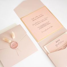 the wedding stationery is set on top of pink envelopes, with a white feather sticking out of it