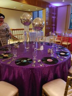 a woman standing next to a purple table with disco balls on it and plates in front of her