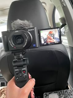 a person holding a camera in the back seat of a car with a microphone attached to it