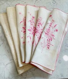 four pink embroidered napkins sitting on top of a marble countertop next to each other