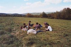 a group of people sitting on top of a grass covered field next to each other