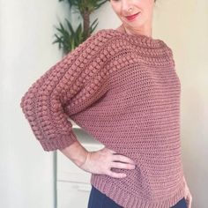 a woman standing in front of a plant wearing a pink sweater