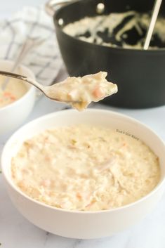 a spoon full of soup is being held by someone's hand over the bowl