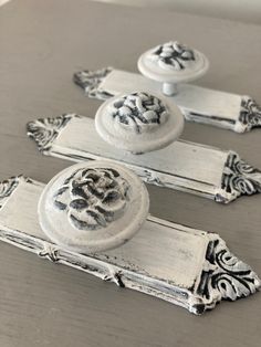 three white cabinet knobs with ornate designs on the front and back sides, sitting on top of a wooden table