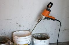 two buckets with paint and a power drill on top of them in front of a white wall