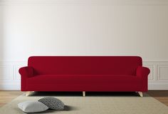 a red couch sitting on top of a wooden floor next to a white wall and rug