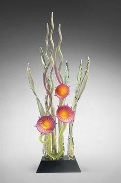 a glass sculpture with flowers and seaweed on a black base in front of a gray background