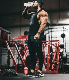 a man drinking from a bottle while standing in a gym with his hands on his hips