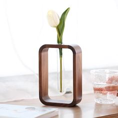 a wooden vase with a flower in it on a table next to a glass cup