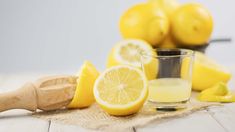 a shot glass filled with lemon juice next to sliced lemons and a wooden spoon