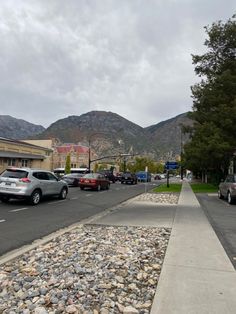 cars parked on the side of a road next to a parking lot with mountains in the background