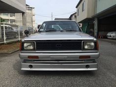 a silver truck parked on the side of a road next to a building and another car