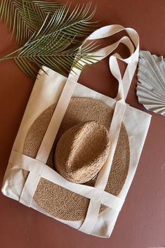 a straw hat sits on top of a canvas tote bag next to a fan